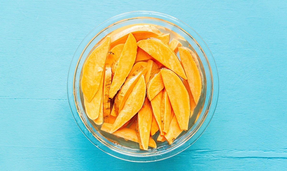 A clear glass bowl filled with water and soaking sweet potato wedges