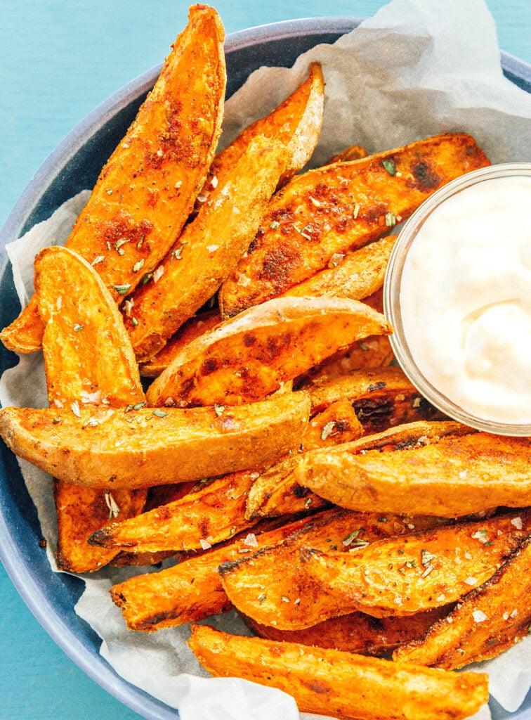 A blue bowl filled with oven-baked sweet potato wedges and a small bowl of garlic mayo sauce