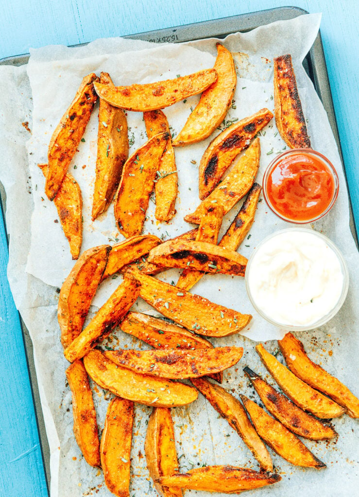 A baking tray line with parchment paper and a layer of cooked oven-baked sweet potato wedges with garlic mayo sauce