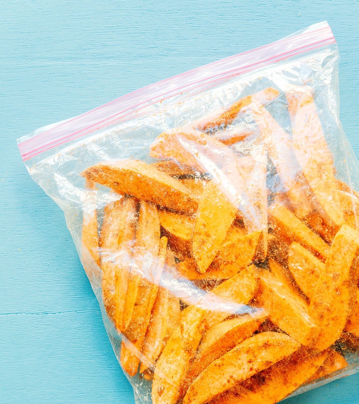 A Ziploc bag filled with sweet potato wedges and coated in olive oil and seasonings