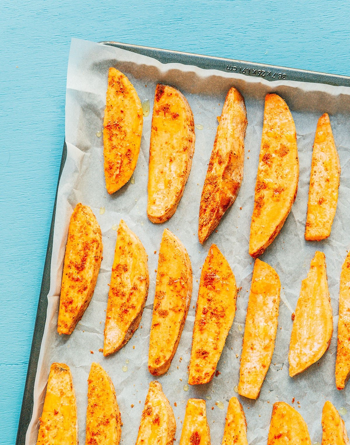 A baking sheet lined with parchment paper and a neat layer of sweet potato wedges