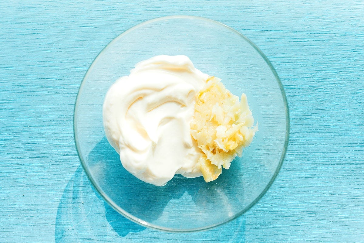 A clear glass bowl filled with mayo, roasted garlic, and lemon juice