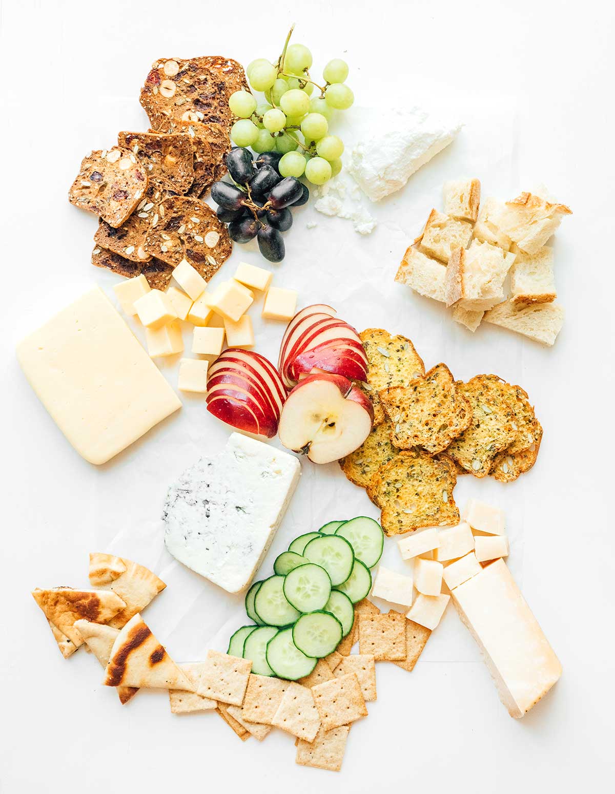 A charcuterie board that is coming together with crackers, breads, fruits, veggies, and cheeses