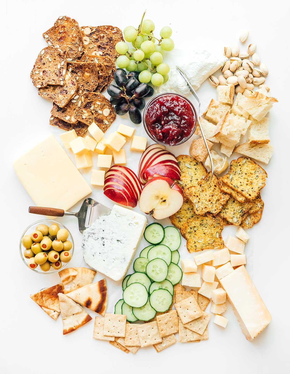 A cheese board complete with various crackers, cheeses, fruits, veggies, spreads, nuts, and olives