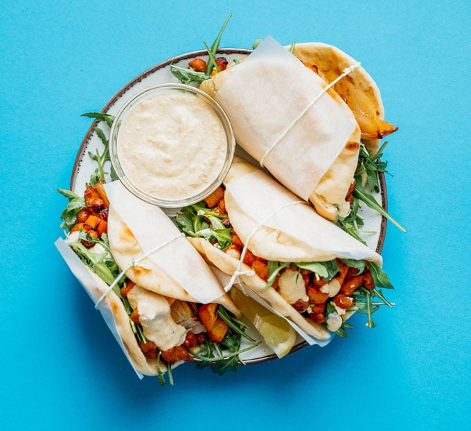 Butternut wraps on a plate with blue background - Spicy, savory flavor all wrapped up in warm flatbreads is the name of the game with these Roasted Butternut Chickpea Hummus Wraps!