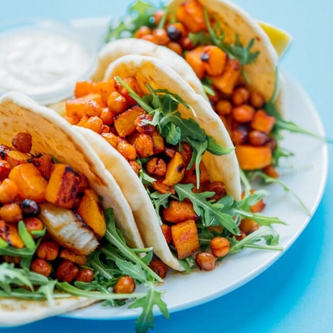 Butternut wraps on a plate with blue background - Spicy, savory flavor all wrapped up in warm flatbreads is the name of the game with these Roasted Butternut Chickpea Hummus Wraps!
