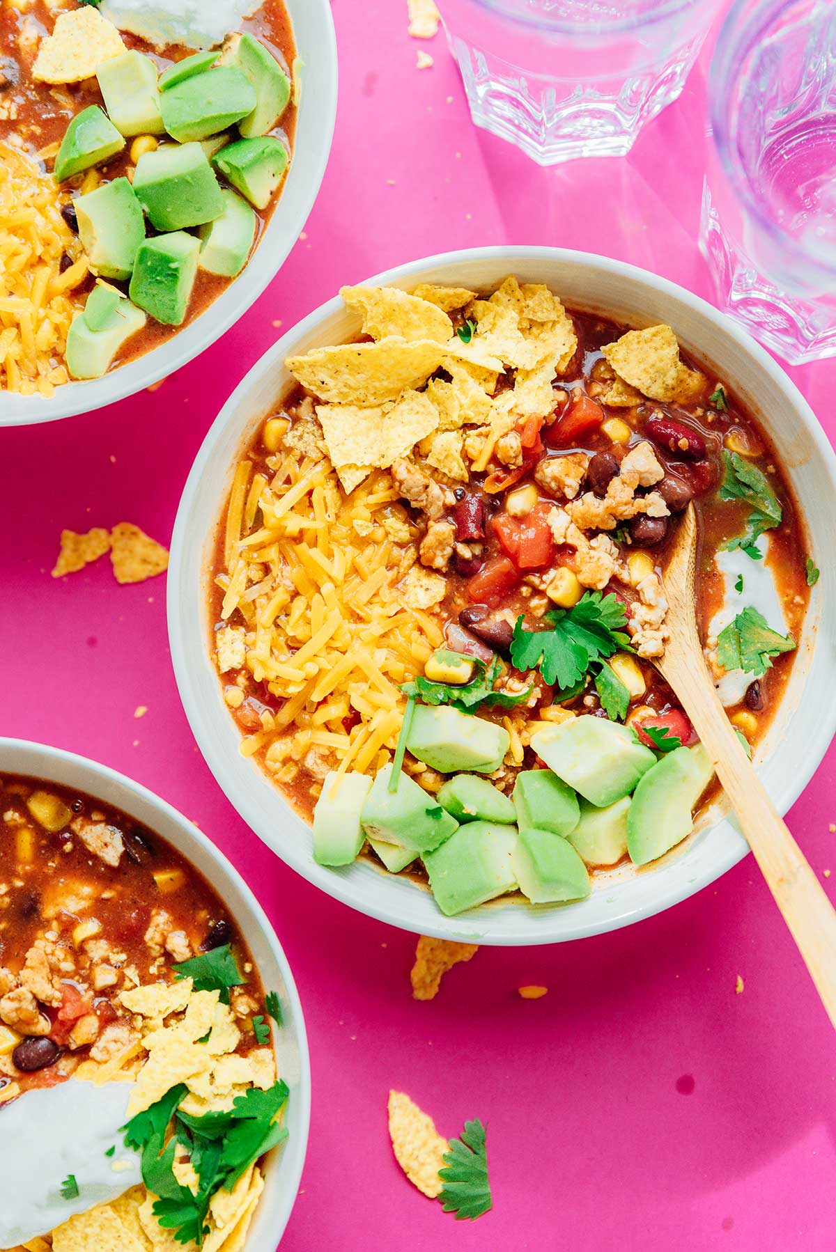 Taco soup in a bowl on a pink background topped with avocado and chips