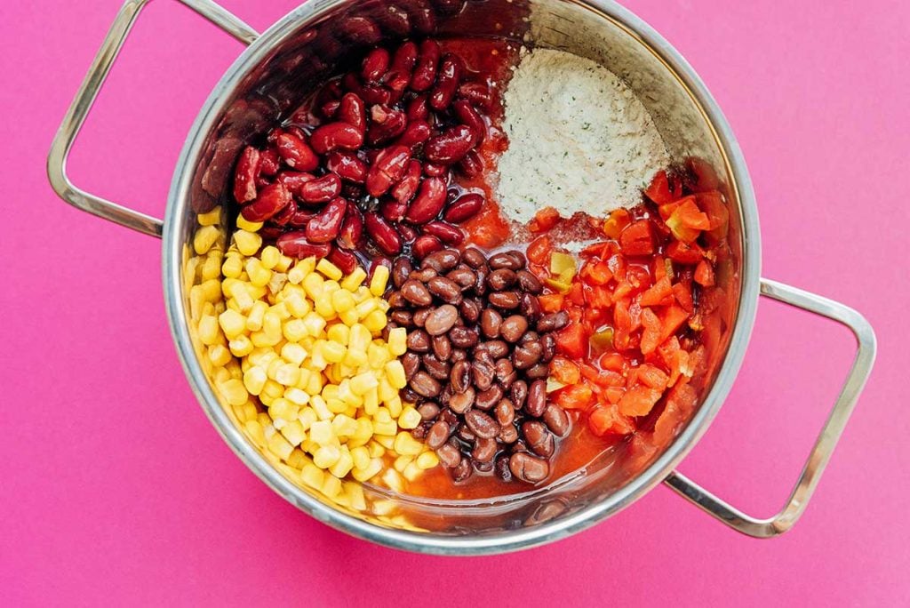 Beans, corn, and tomatoes in a pan on a pink background