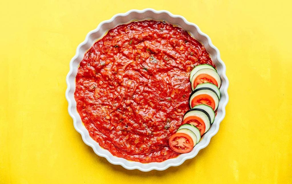 Layering raw vegetables in a tart pan with tomato sauce on botton