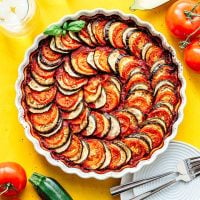 Layered vegetable tian in a tart pan on a yellow background