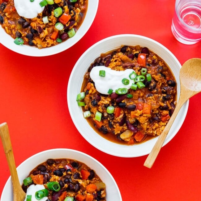 Vegan tempeh chili in white bowls on a red background