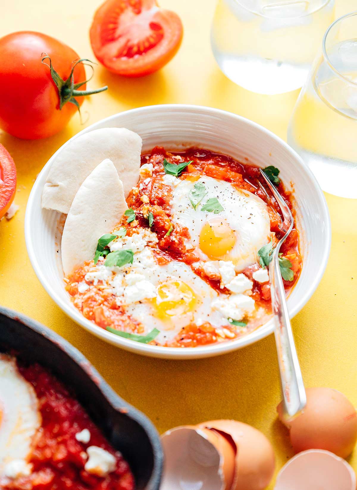 Shakshuka with eggs and pita break in a bowl on a yellow background