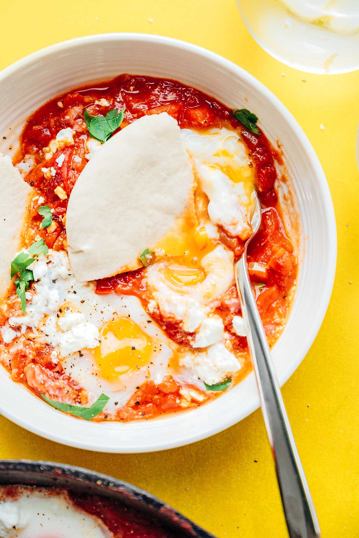 Close up shakshuka with eggs and pita break in a bowl on a yellow background