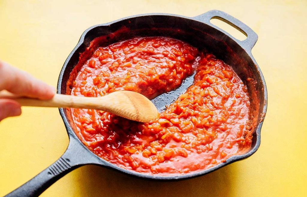 Thick tomato sauce in a cast iron skillet on a yellow background