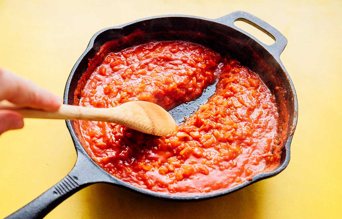 Thick tomato sauce in a cast iron skillet on a yellow background