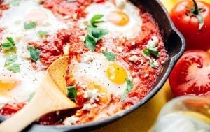 Close up photo of cooked eggs in tomato sauce in a cast iron skillet on a yellow background