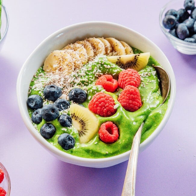 Green smoothie bowl with fruit and a spoon.