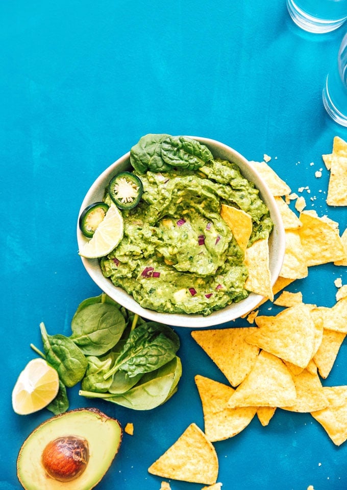 Healthy guacamole in a bowl with tortilla chips spinach