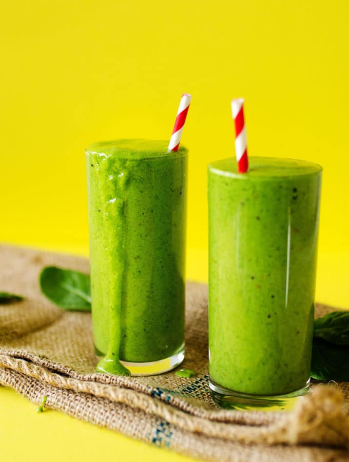 Green smoothie picture in a glass with a striped straw and a yellow background