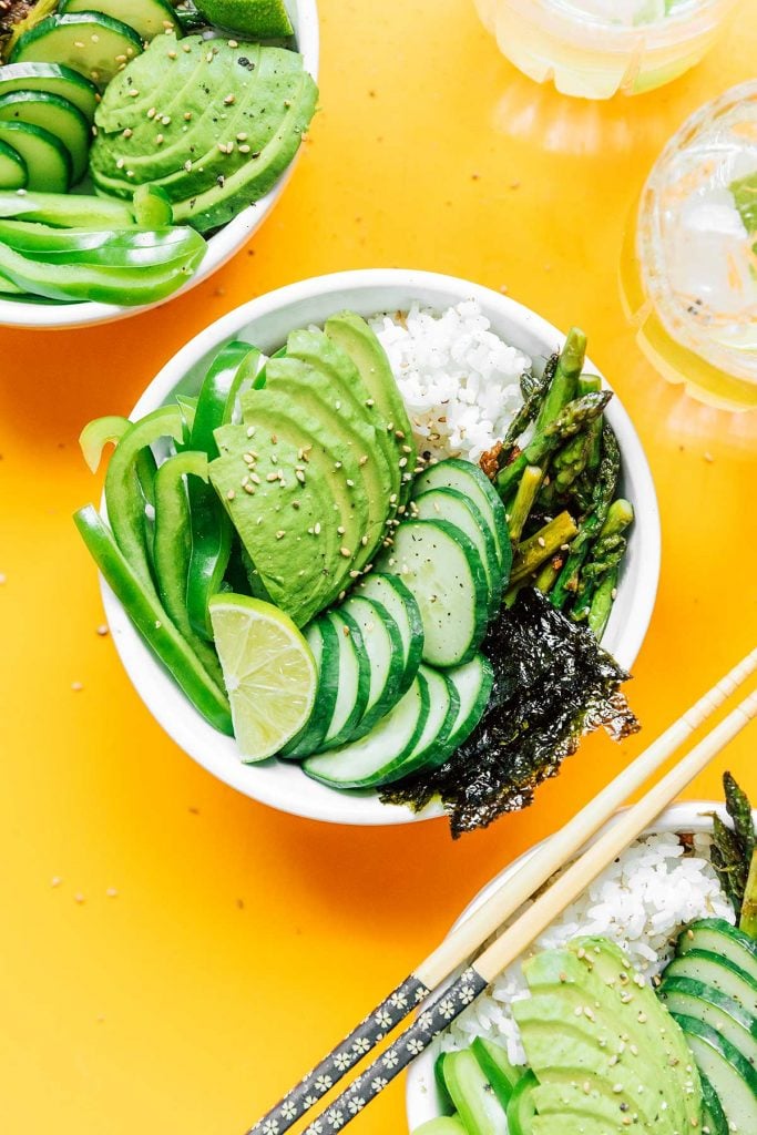 A complete green goddess sushi bowl containing rice, asparagus, sushi paper, cucumber, avocado, green bell pepper, and lime