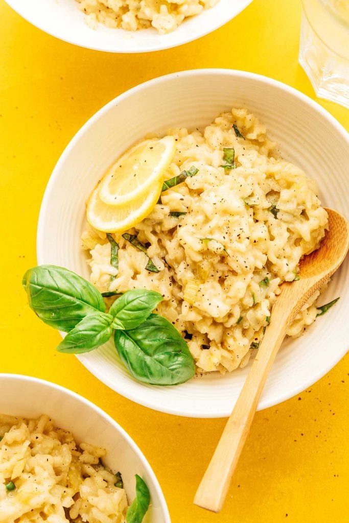 Lemon risotto in a bowl with a spoon and basil on a yellow background