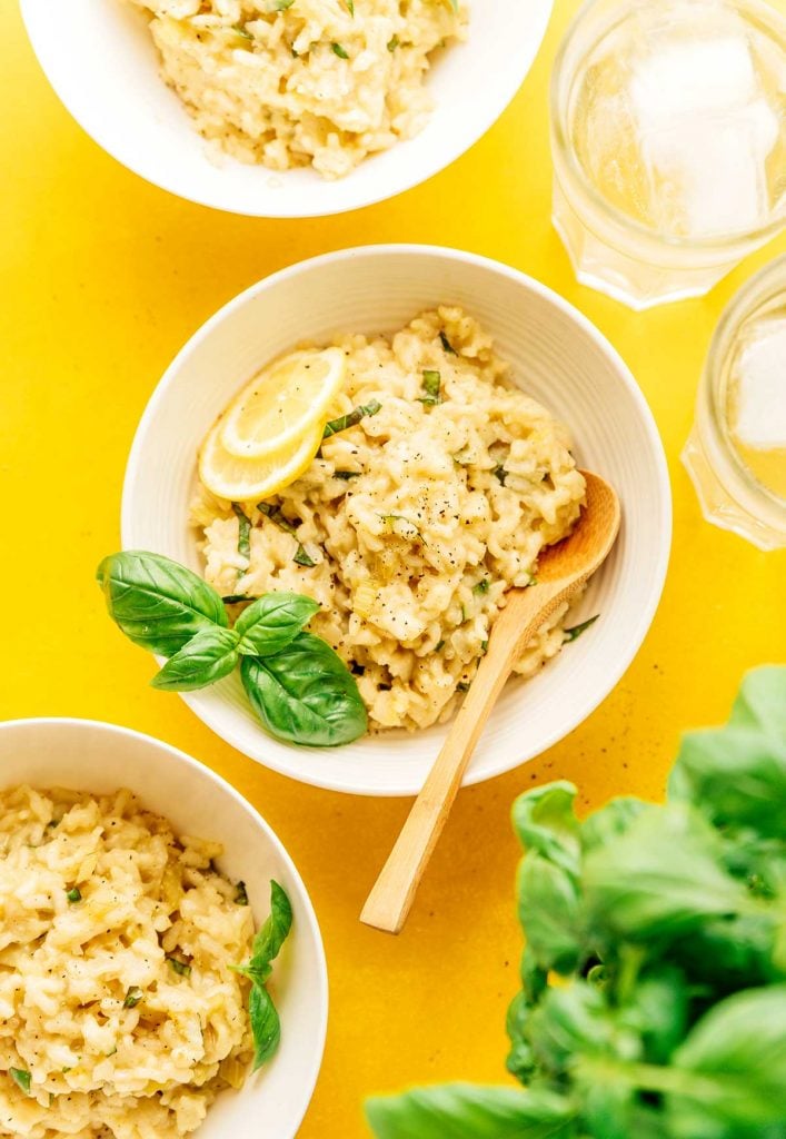 Lemon risotto in a bowl with a spoon and basil on a yellow background