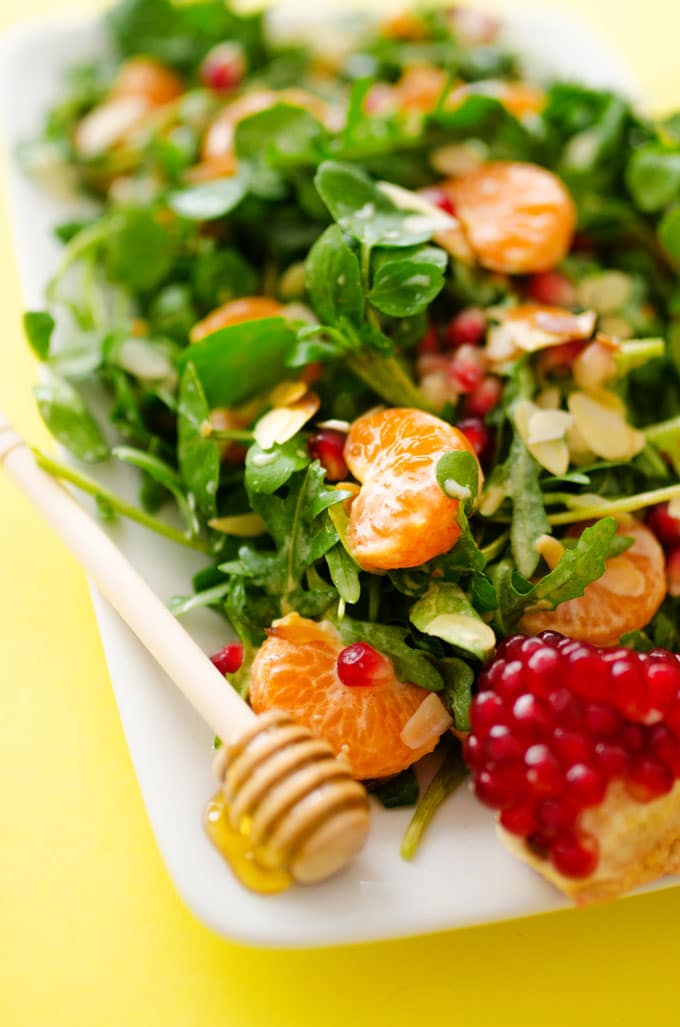 Watercress salad with orange and pomegranate on a yellow background