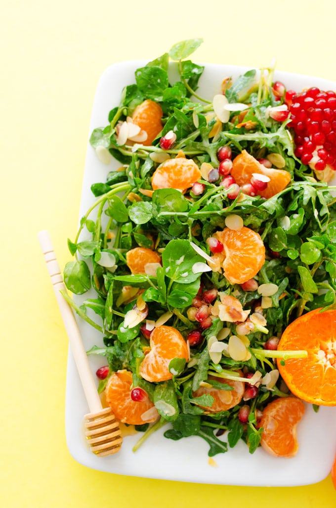 Watercress salad with orange and pomegranate on a yellow background