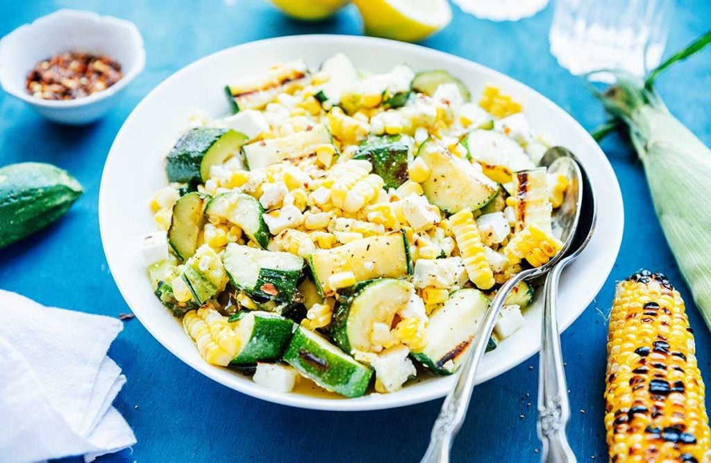 Horizontal photo of zucchini corn salad on a white plate with serving spoons