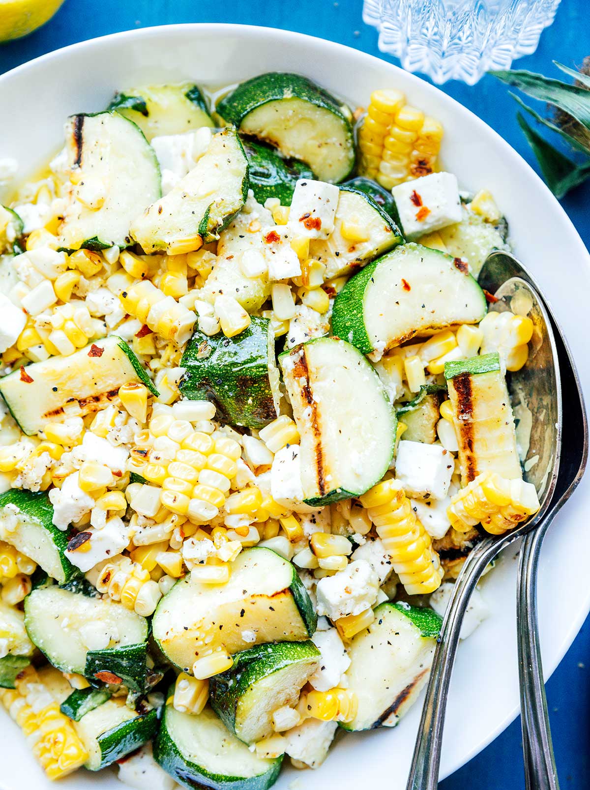 Zucchini corn salad on a white plate with serving spoons.