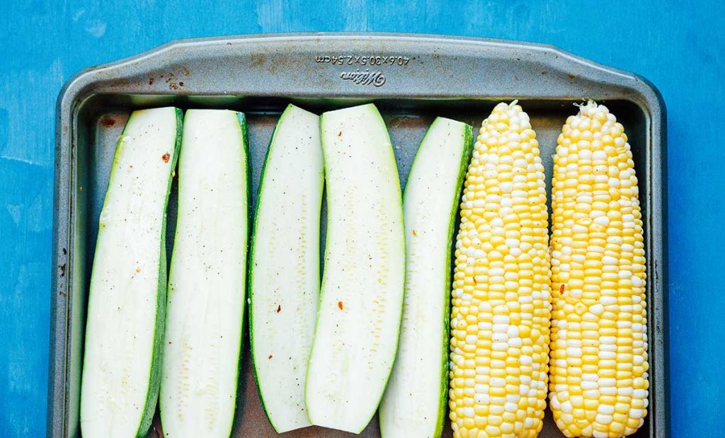 Sliced zucchini and corn on a baking sheet