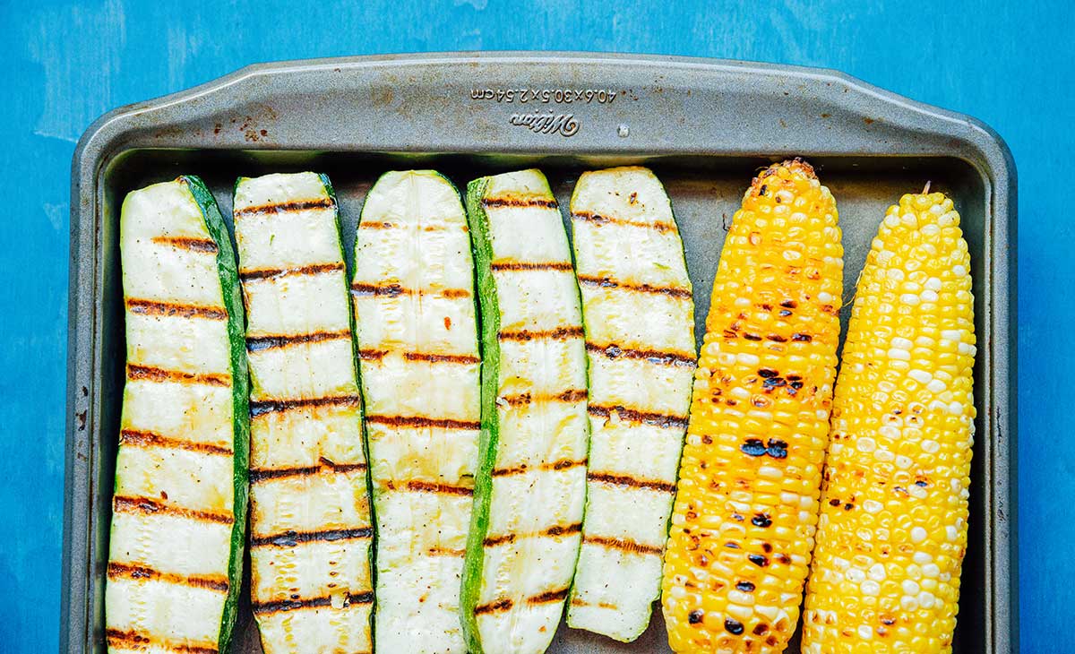 Char grilled zucchini and corn on a baking sheet.