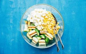 Ingredients to make zucchini corn salad on a white plate with serving spoons