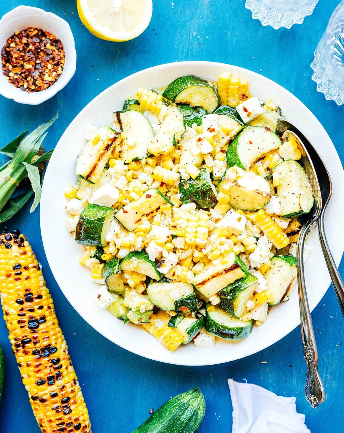 Zucchini corn salad on a white plate with serving spoons.