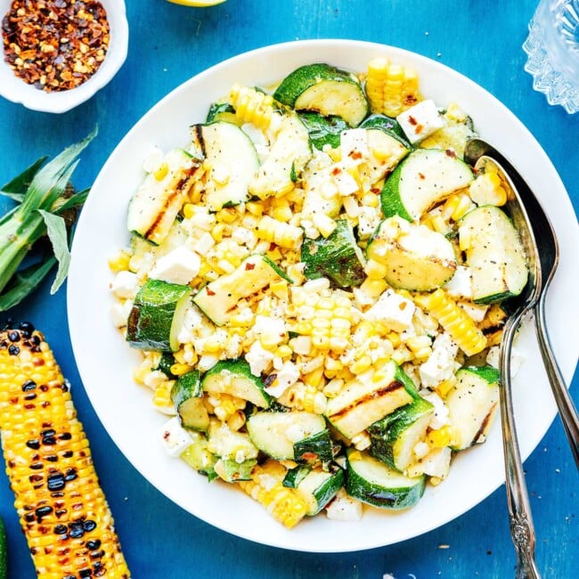 Zucchini corn salad on a white plate with serving spoons