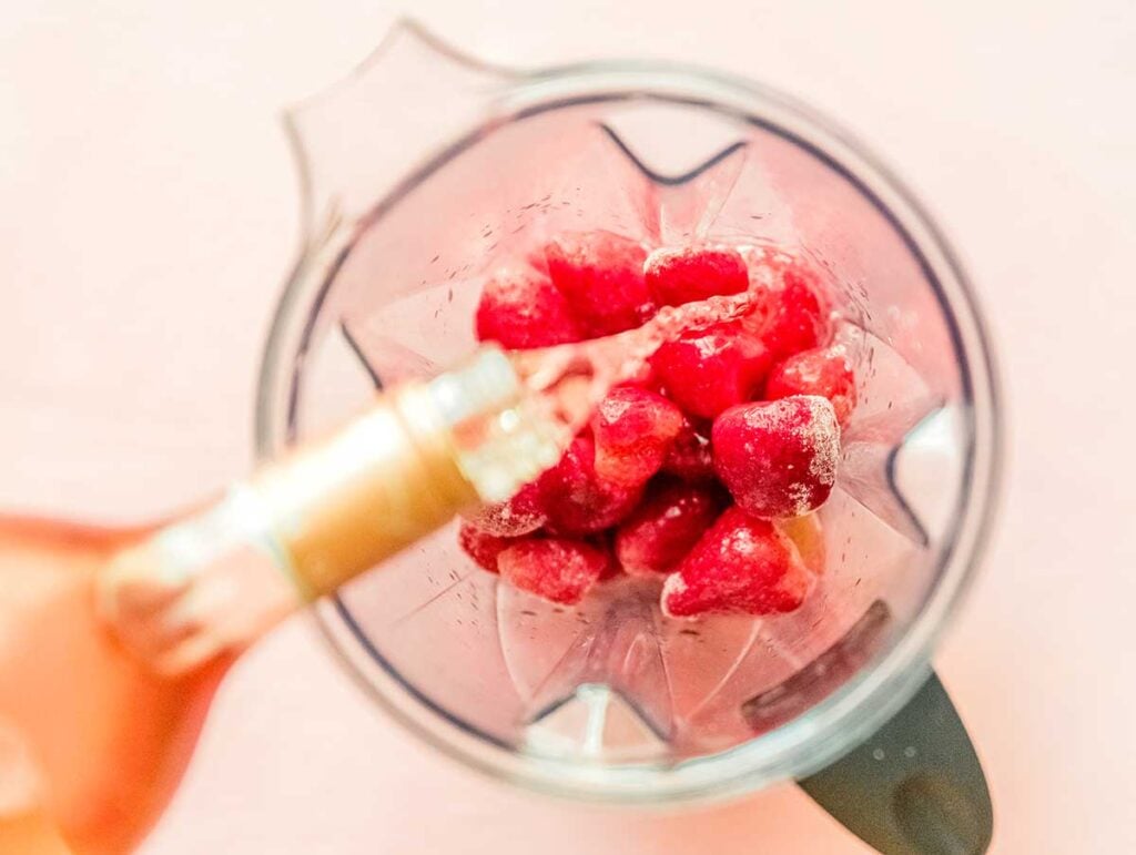 Pouring rosé into a blender filled with frozen strawberries