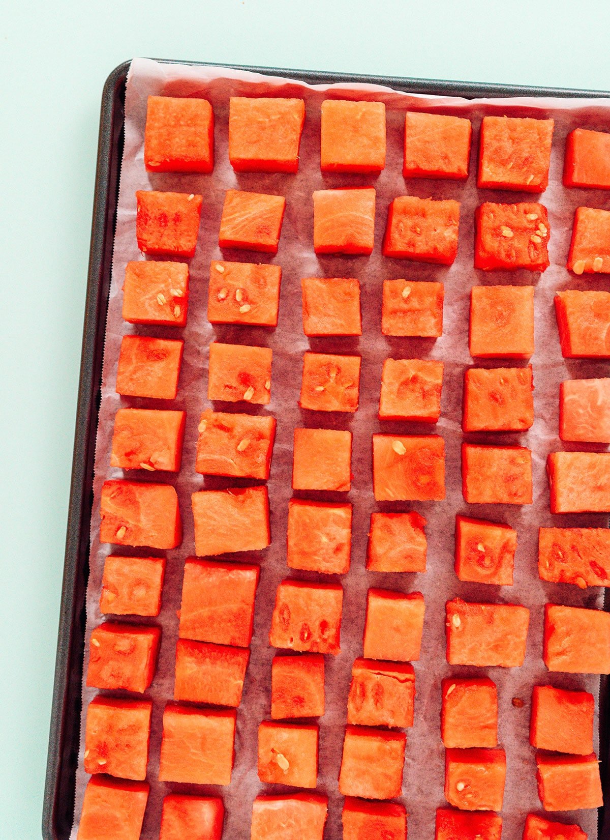 Frozen watermelon cubes on a lined baking tray.
