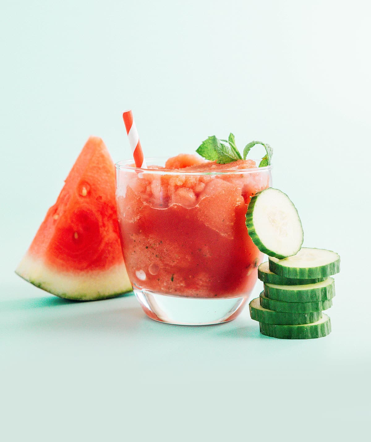 A watermelon smoothie with a stack of cucumbers on one side and a watermelon on the other side.