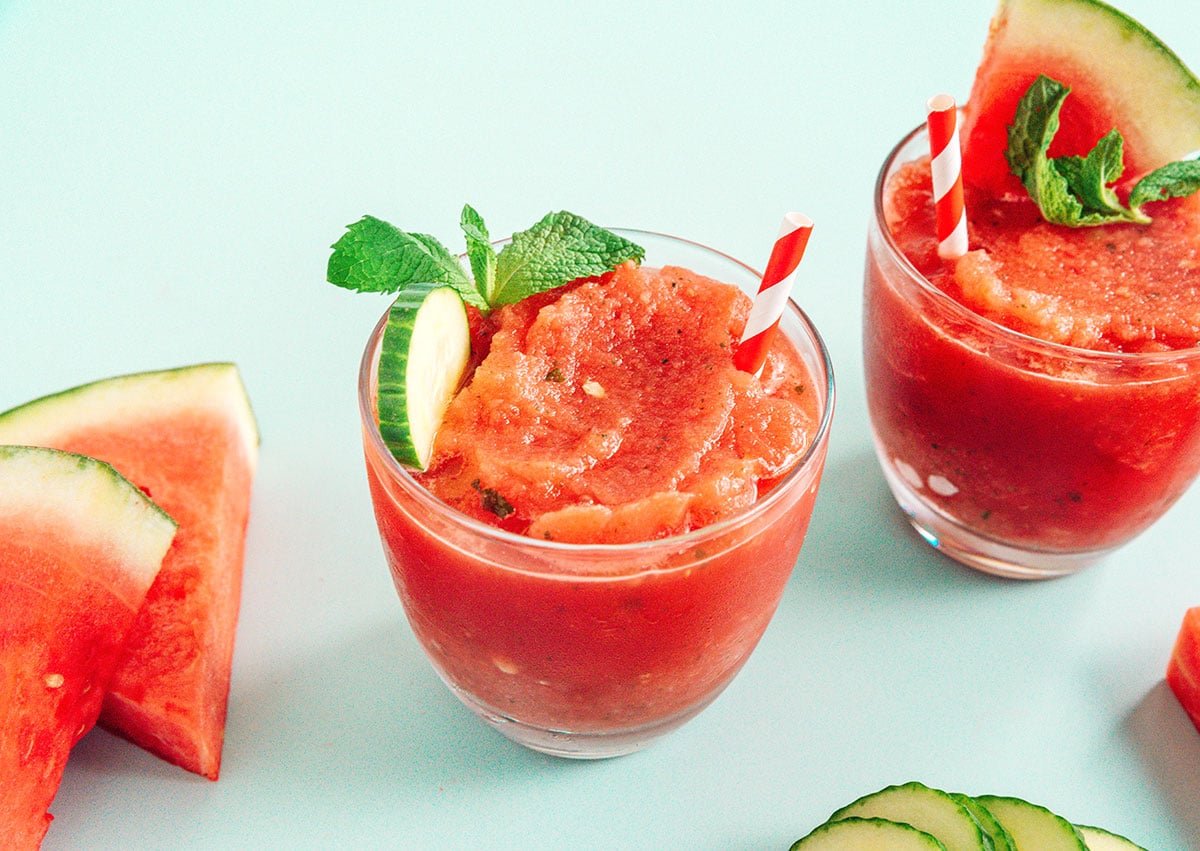 Two watermelon smoothies with red straws and cucumber and mint topping them.