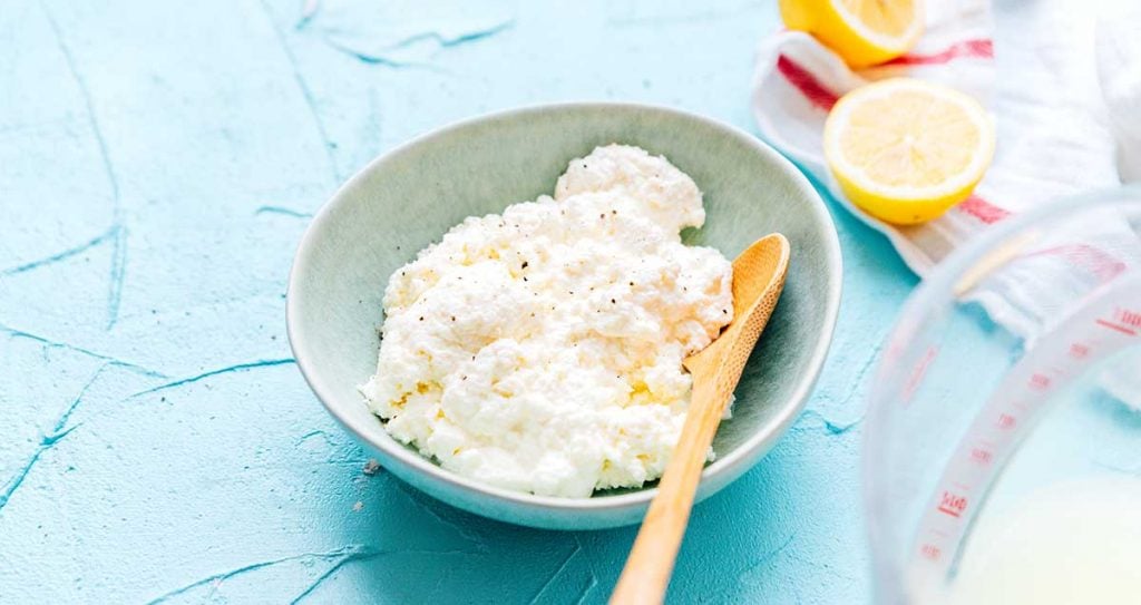 Homemade ricotta cheese in a blue bowl with a spoon