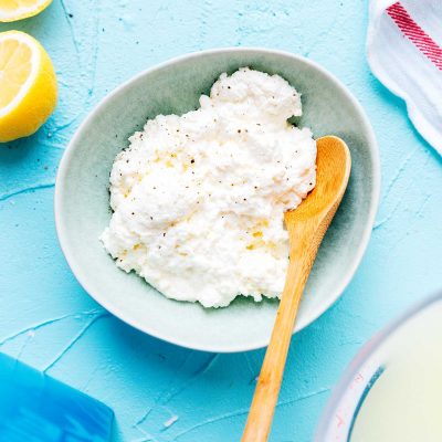 Homemade ricotta cheese in a blue bowl with a spoon