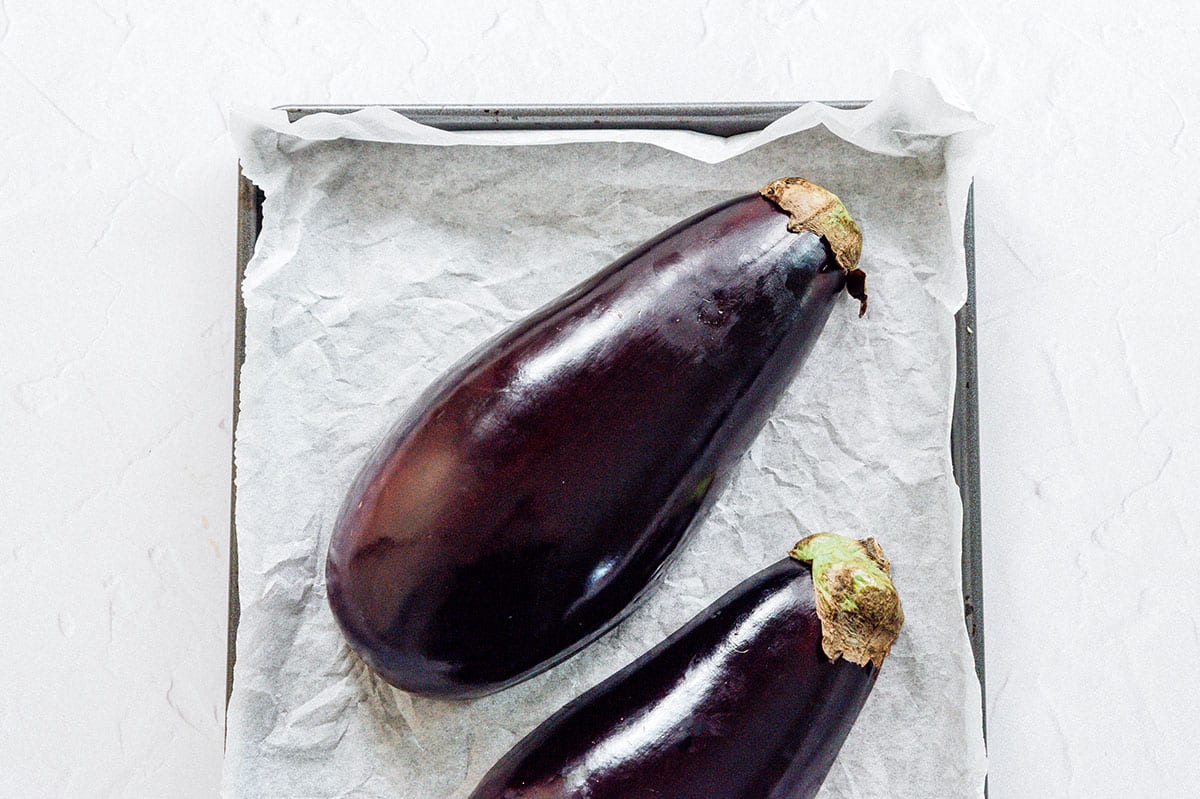 Eggplant cut in half laying face down on a baking tray.