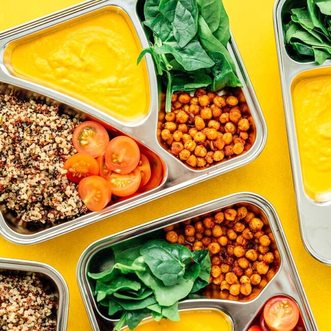 Vegetarian meal prep with roasted chickpeas, quinoa, yellow sauce, and spinach on a yellow background
