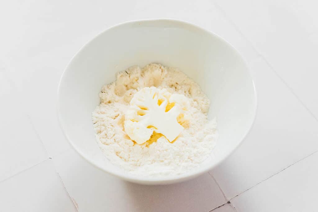 A white bowl filled with flour with one cauliflower floret inside