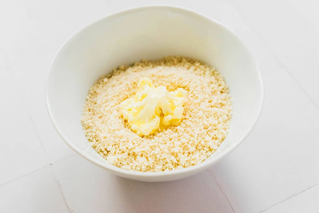 One cauliflower floret being dipped in a white bowl filled with panko breadcrumbs