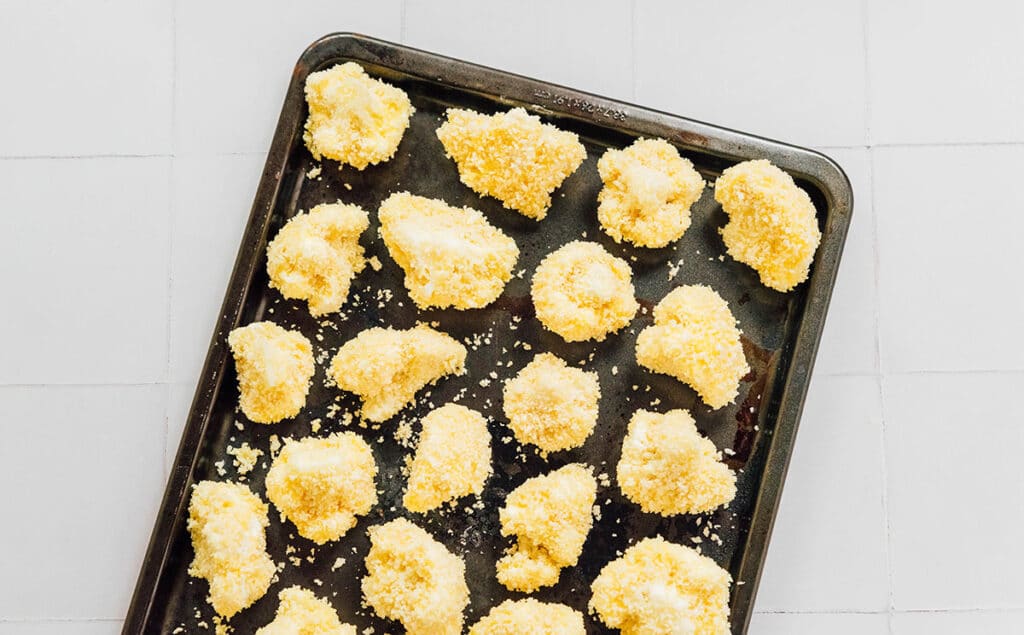 A baking sheet lined with a single layer of breaded cauliflower florets