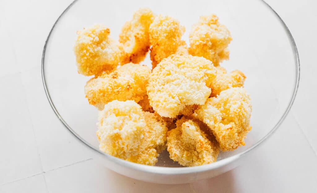 A clear glass bowl filled with breaded cauliflower florets