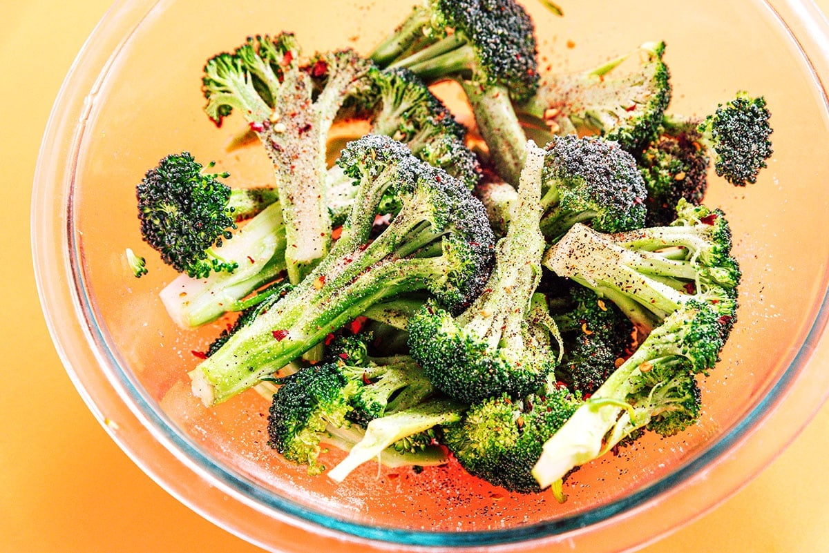 A bowl of raw broccoli with spices and oil added to it.