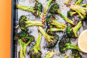 Roasted broccoli florets on a baking sheet with grated cheese, savory seasoning, and a lemon wedge on the side create a delicious roasted broccoli dish.