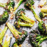 Close-up of roasted broccoli florets on a baking sheet, perfectly seasoned with grated cheese, black pepper, and salt.
